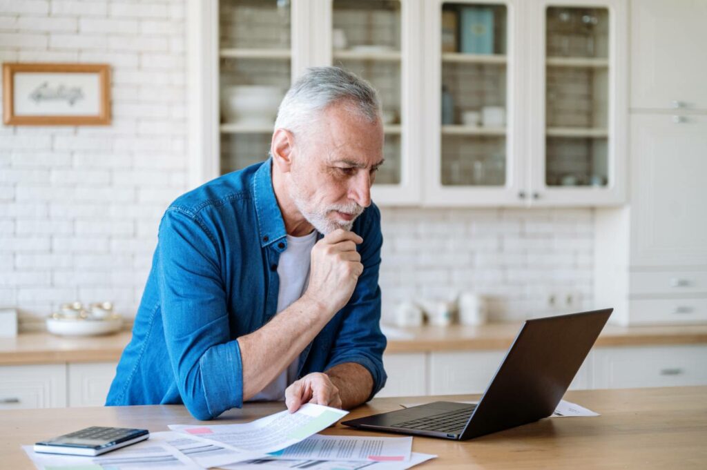 Bildet viser en eldre mann som sitter og leser på den bærbare datamaskinen sin.